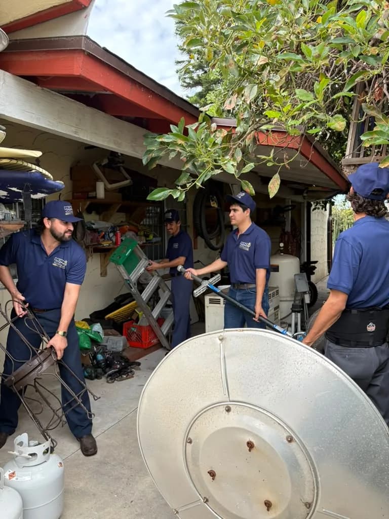 Mundo Junk Removal & Recycling crew clearing a garage — a lawn mower, a step ladder, propane tanks and an old fan