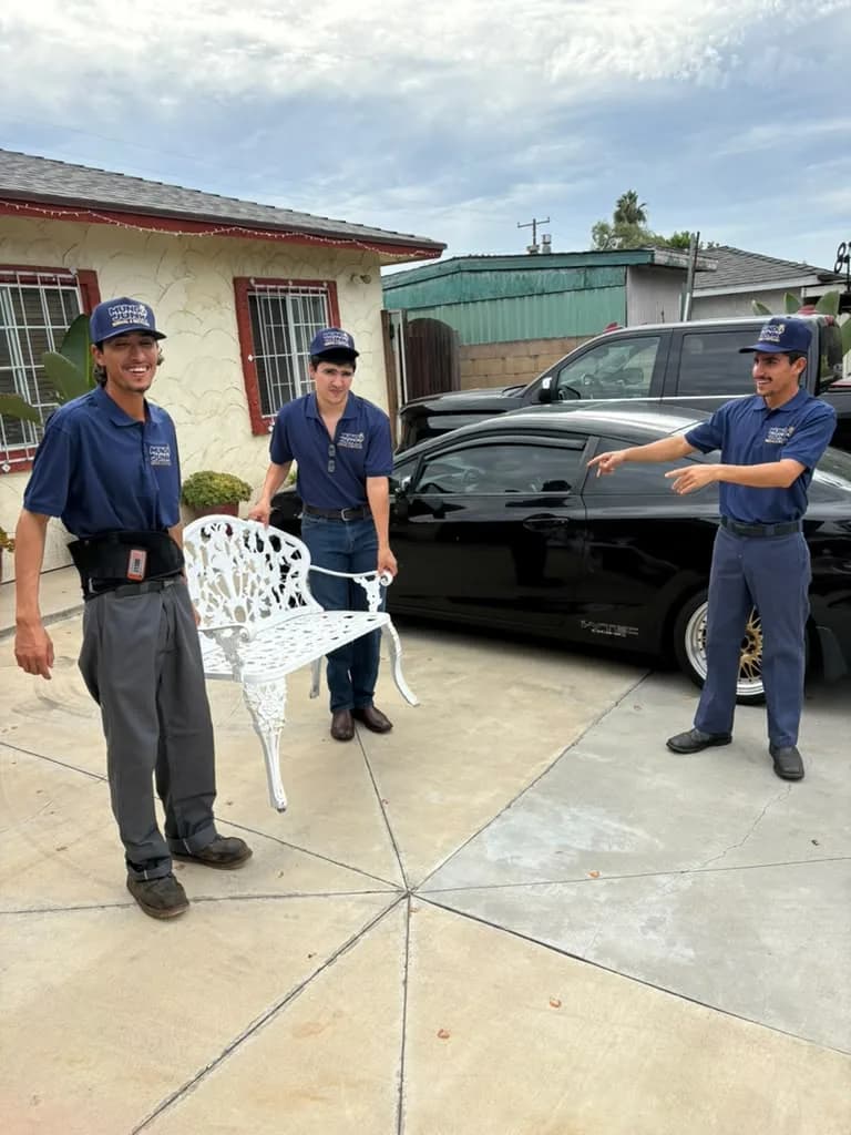 Mundo Junk Removal & Recycling crew carrying a cast iron patio bench out of a driveway